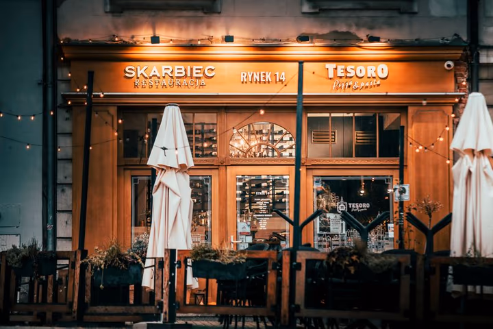 Façade chaleureuse du restaurant Skarbiec avec sa terrasse extérieure illuminée, invitant les clients à s'installer en soirée.